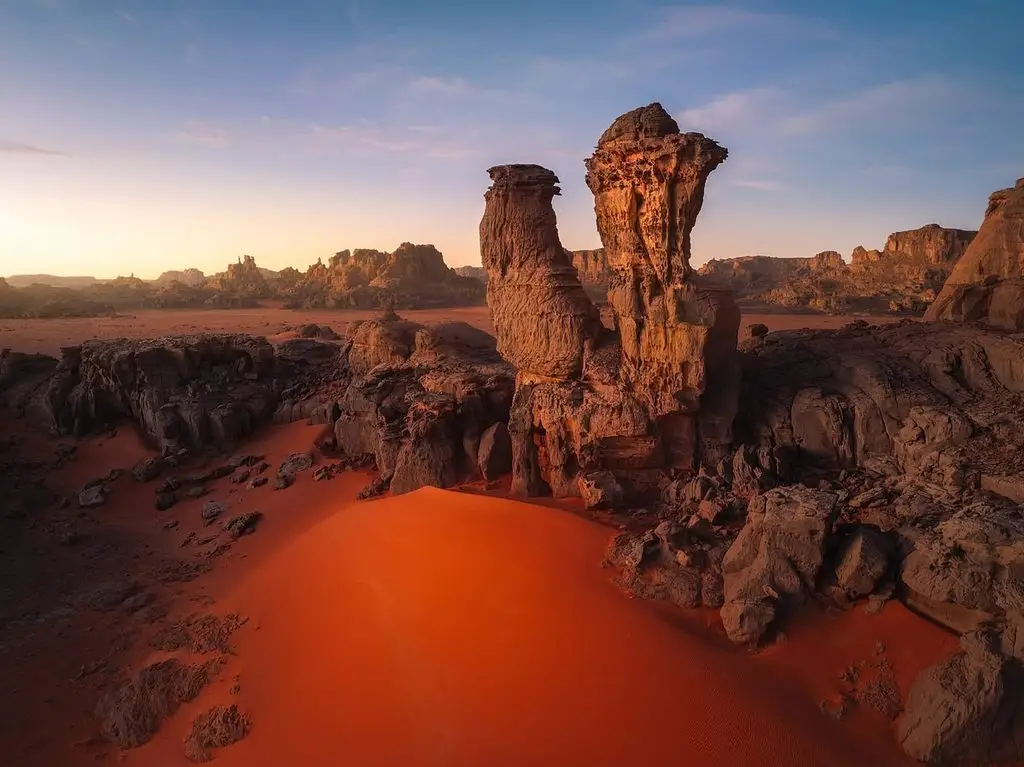 Golden sand dunes against red sandstone rock in Tadrart Rouge, Algeria, at sunset