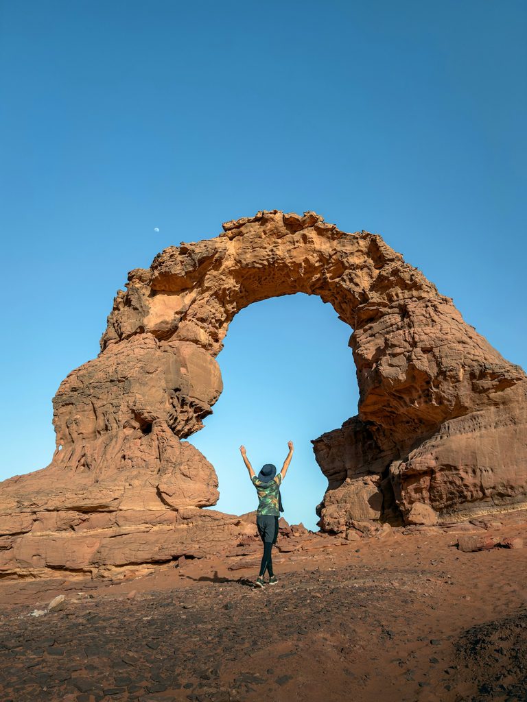 A traveler standing beneath a natural sandstone rock arch near Djanet, Algeria