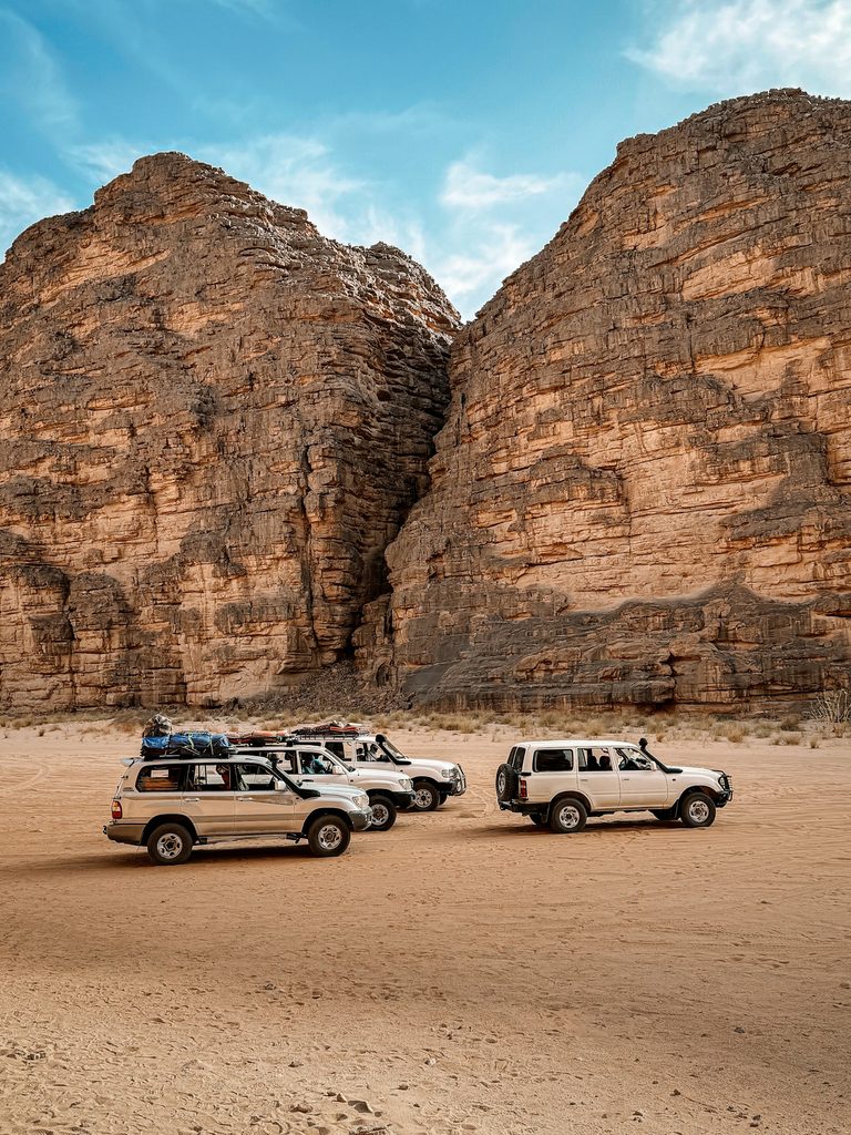 Four-wheel-drive expedition vehicles parked in a desert canyon near Djanet, Algeria