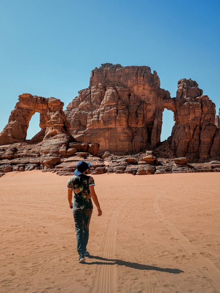 A lone traveler walking across a sandy field next to a rock formation near Djanet, Algeria